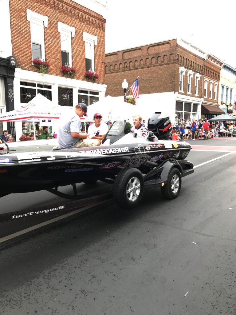 Campbellsville University's bass fishing team was represented in the parade by, from left: Justin Mayfield of Somerset, Ky., and incoming freshmen Ezra Oliver of Campbellsville and Tanner Barnes of Campbellsville, step-son of Megan Barnes, coordinator of introductory studies early alert system at the university. Pulling the boat were team members Colby Hays of Somerset and Travis Hunt of Campbellsville. (Campbellsville University Photo by Joan C. McKinney)