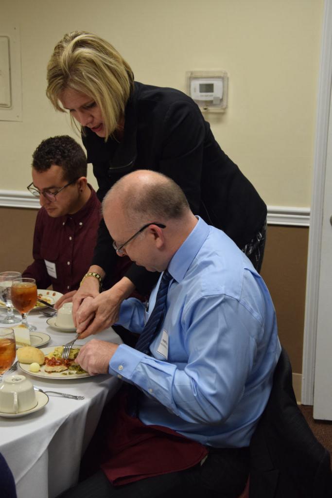 Terri Thompson, shows David Simpson, left, a business administration major from Edmonton, Ky., and Diego Cardenas, a senior art/graphic design student from Venezuela, how to cut their entrée at the dining etiquette dinner. (Campbellsville University Photo by Kasey Ricketts)